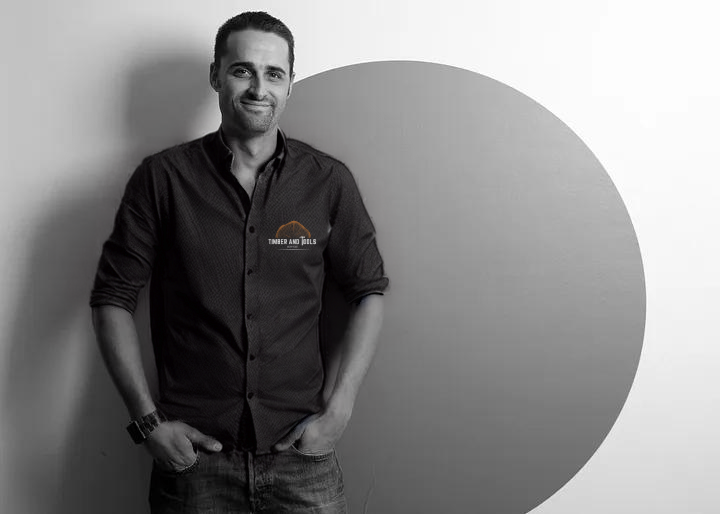 A portrait image of owner Dominic Watts, wearing a black shirt with timber and tools logo