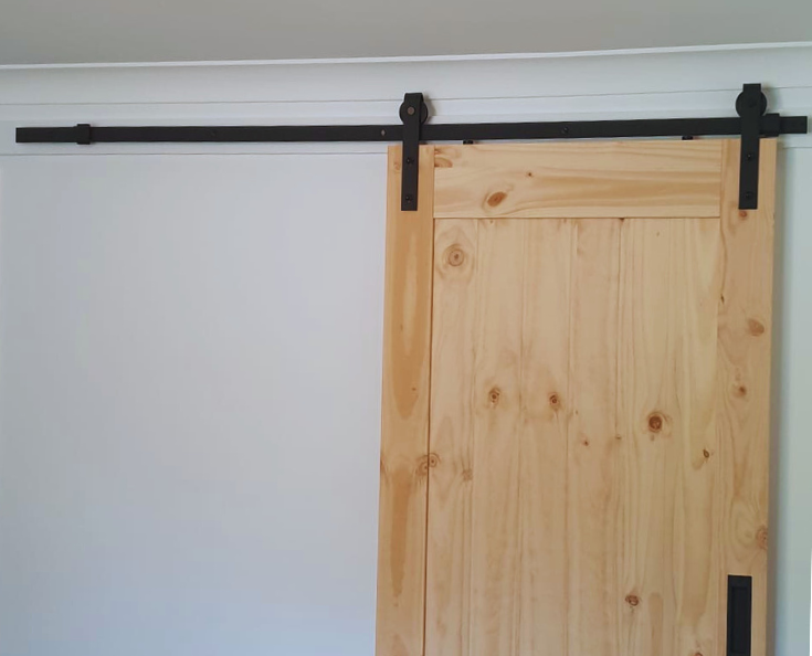 A timber barn door on black fixings against a white wall