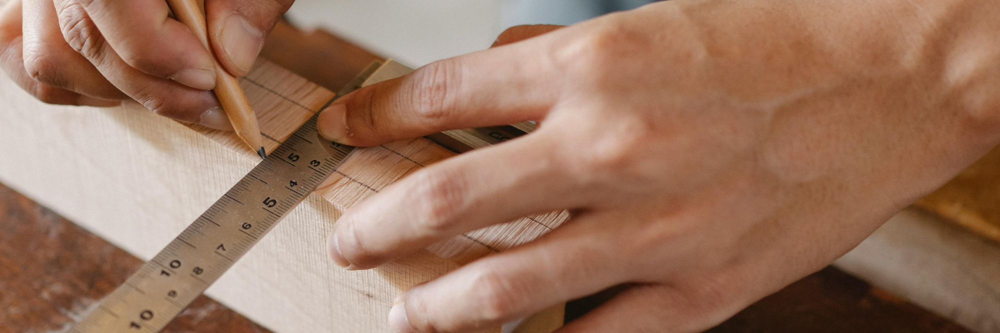 An image of someones hands measuring against a ruler on wood