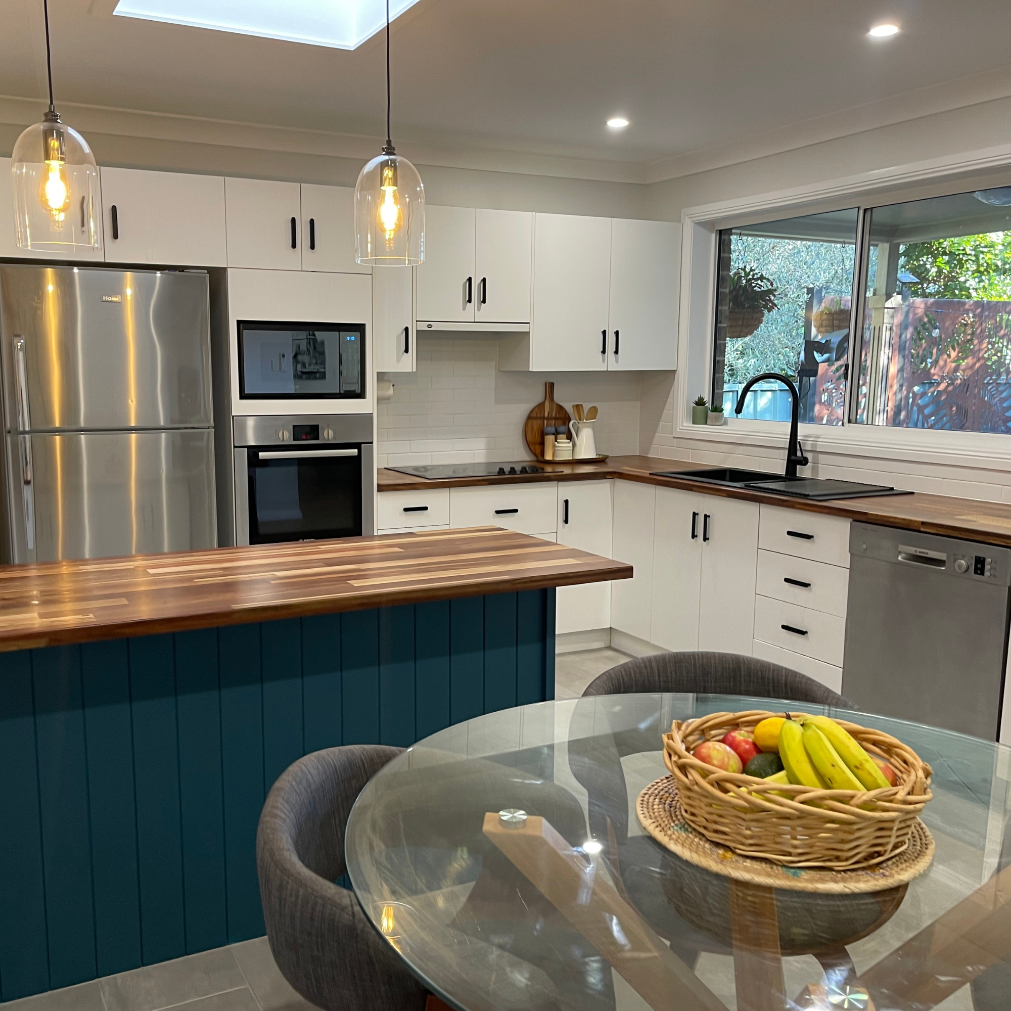 An image of a kitchen with timber bench tops, hanging lights and cabinetry