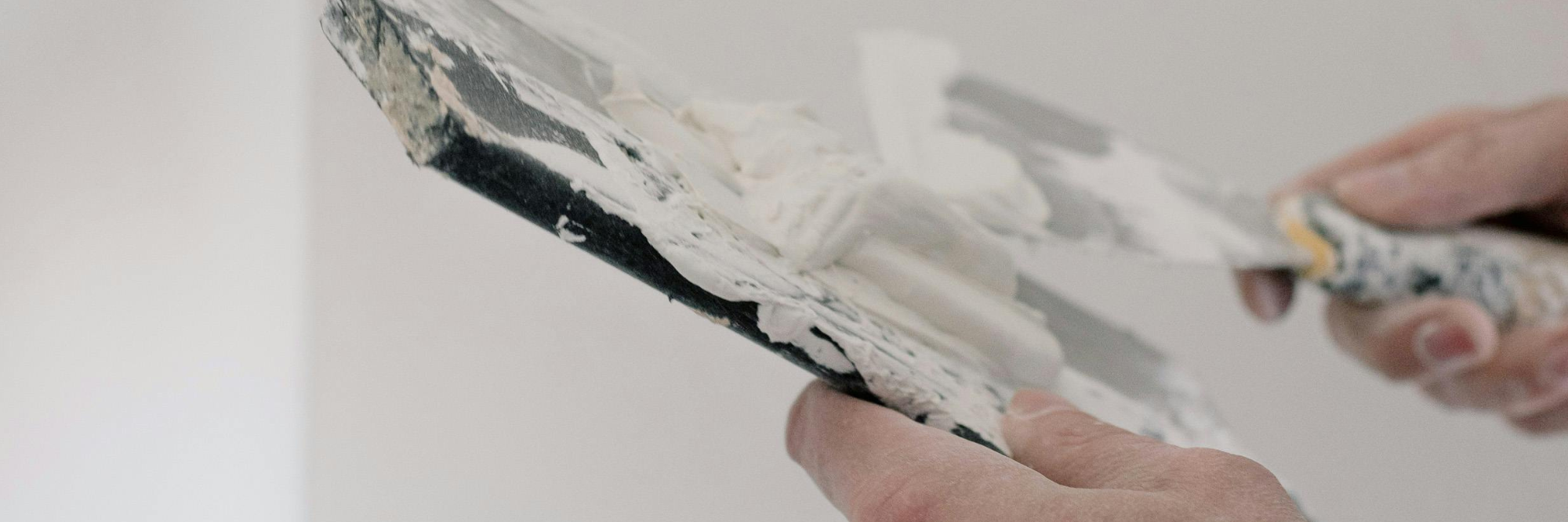 A close up image of someones hands holding a paint brush with white paint in a tray